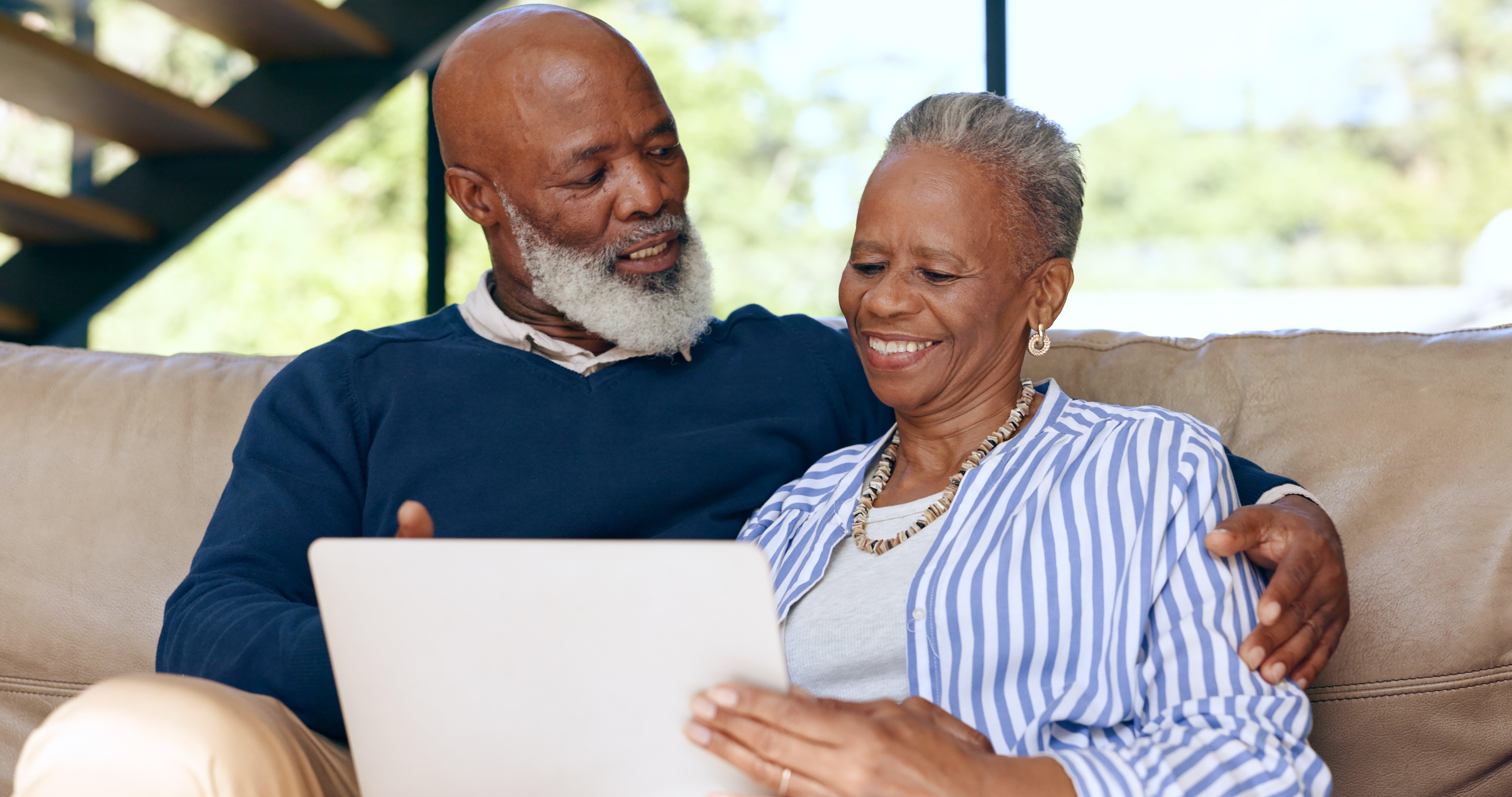 Elderly couple siting on couch talking and looking at tablet
